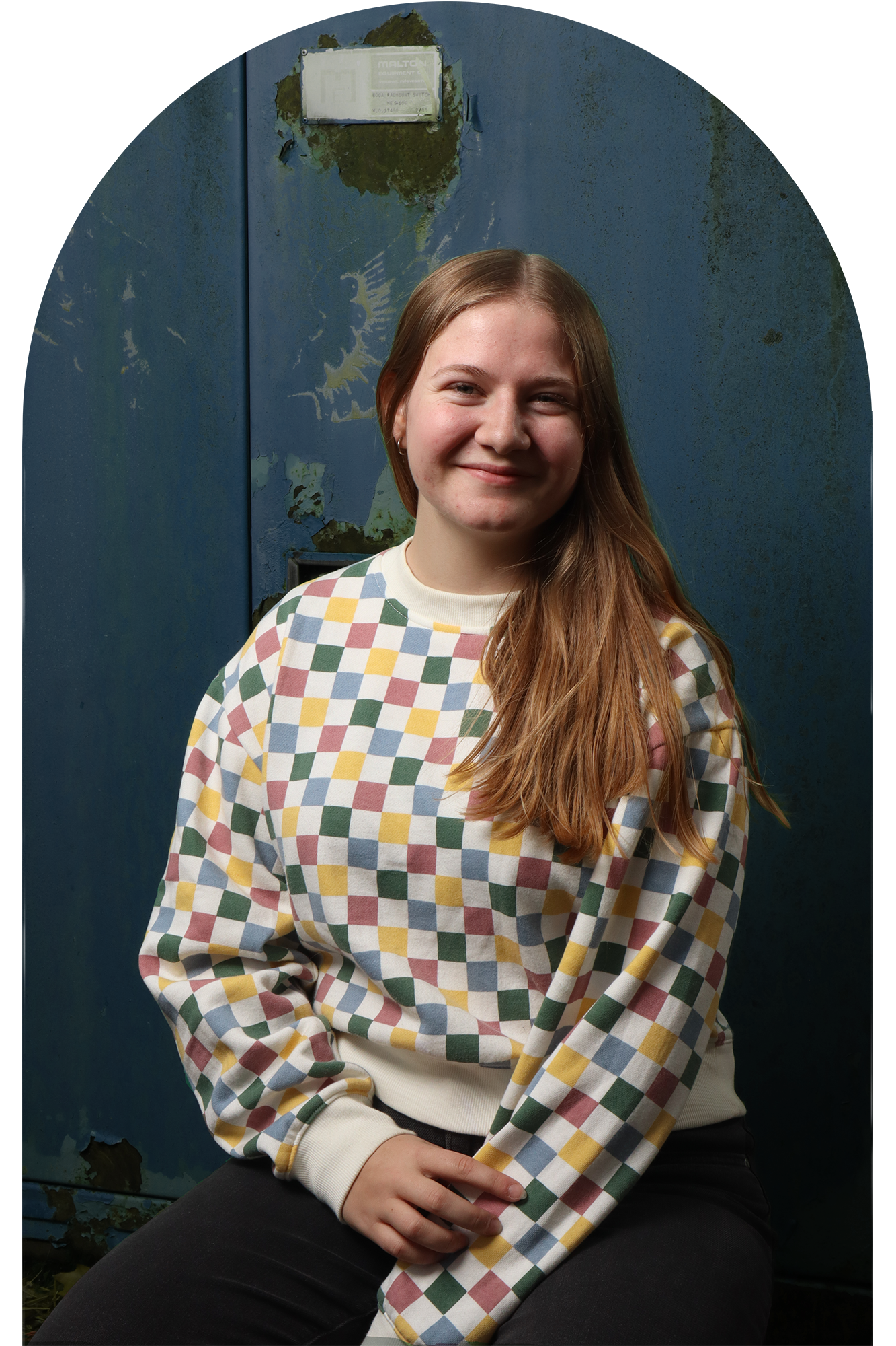 headshot of the artist in a checkered sweater in front of a rustic blue wall
